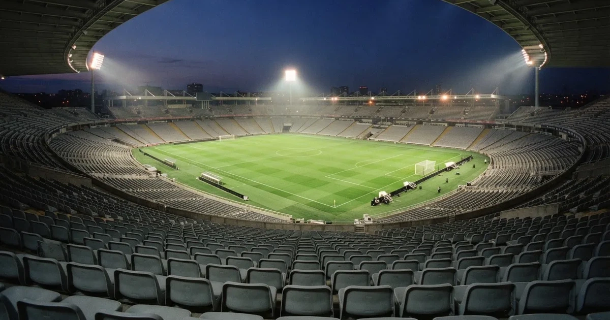Leere Sitzreihen eines großen Stadions unter Flutlicht, dahinter die ferne Sicht auf den hell beleuchteten Rasen nach Sonnenuntergang.