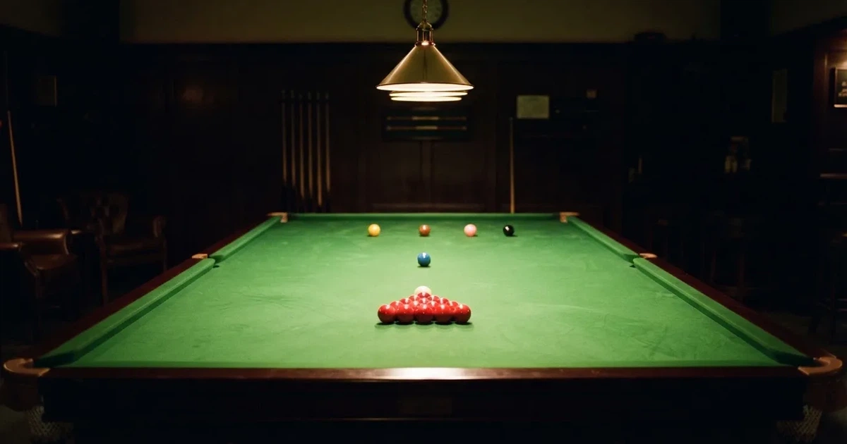 Ein Snookertisch mit grünem Tuch und aufgebauten roten Kugeln in einem abgedunkelten Raum unter einer hängenden Lampe.