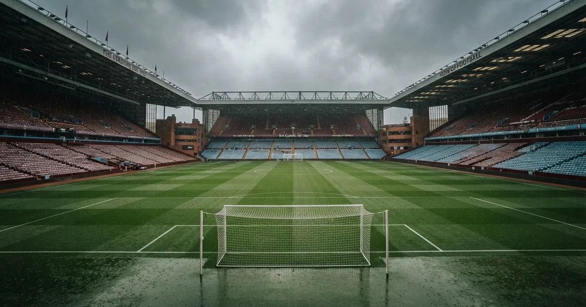Ein englisches Fußballstadion mit rotbraunen Backsteintribünen unter bedecktem Himmel, davor ein nasser Rasen mit Spielfeldlinien.